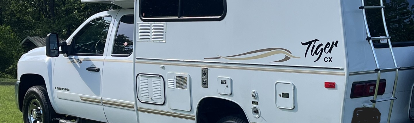 White Tiger CX motorhome parked on a grassy field with trees in the background on a sunny day.