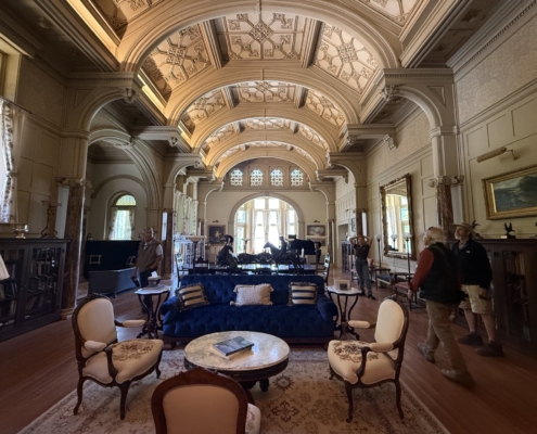 Grand hall with ornate vaulted ceiling, arches, marble columns, and visitors browsing antique furnishings around a blue sofa set.
