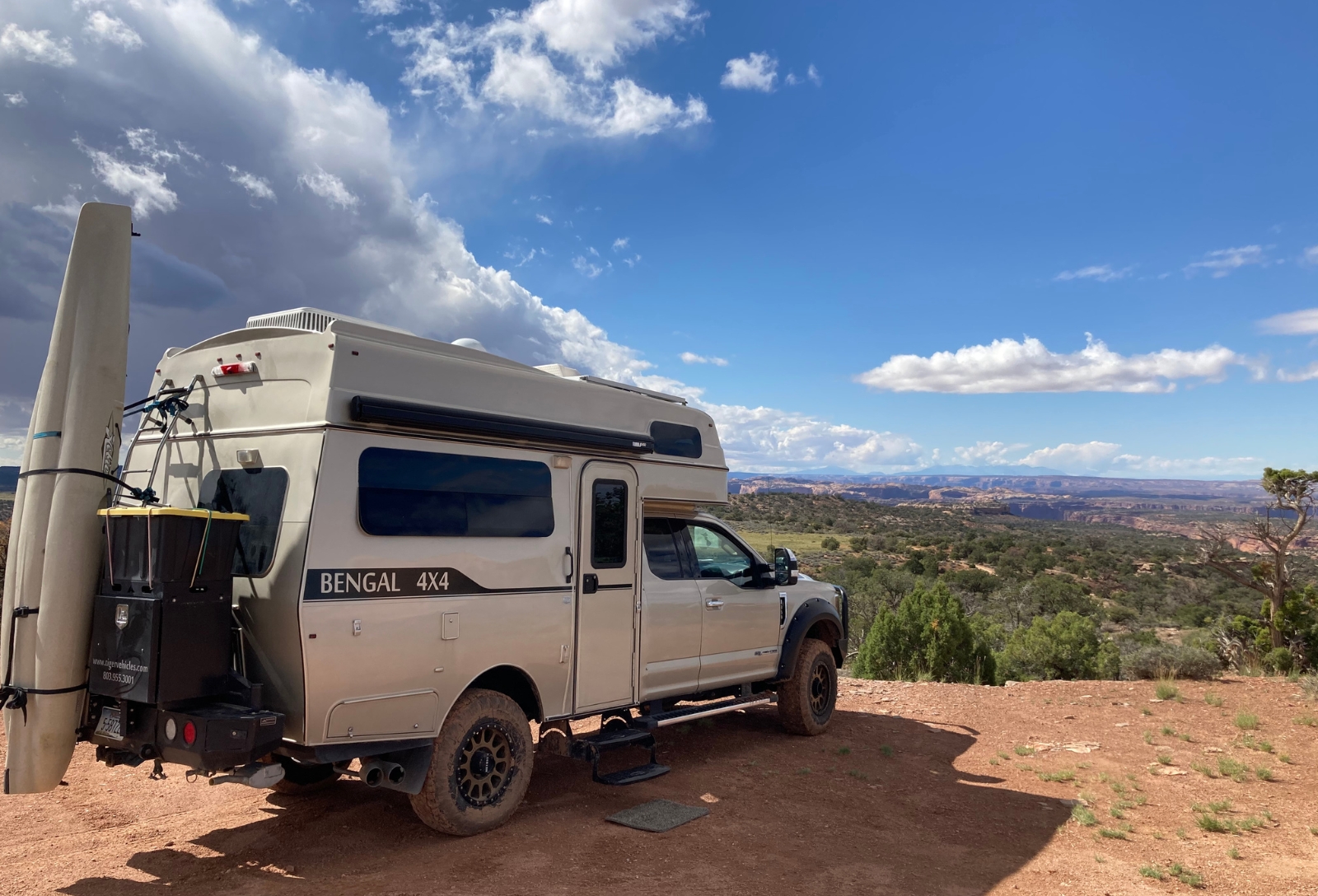 White Bengal 4x4 camper van parked on a dirt overlook, desert canyon and blue sky with clouds in the distance.
