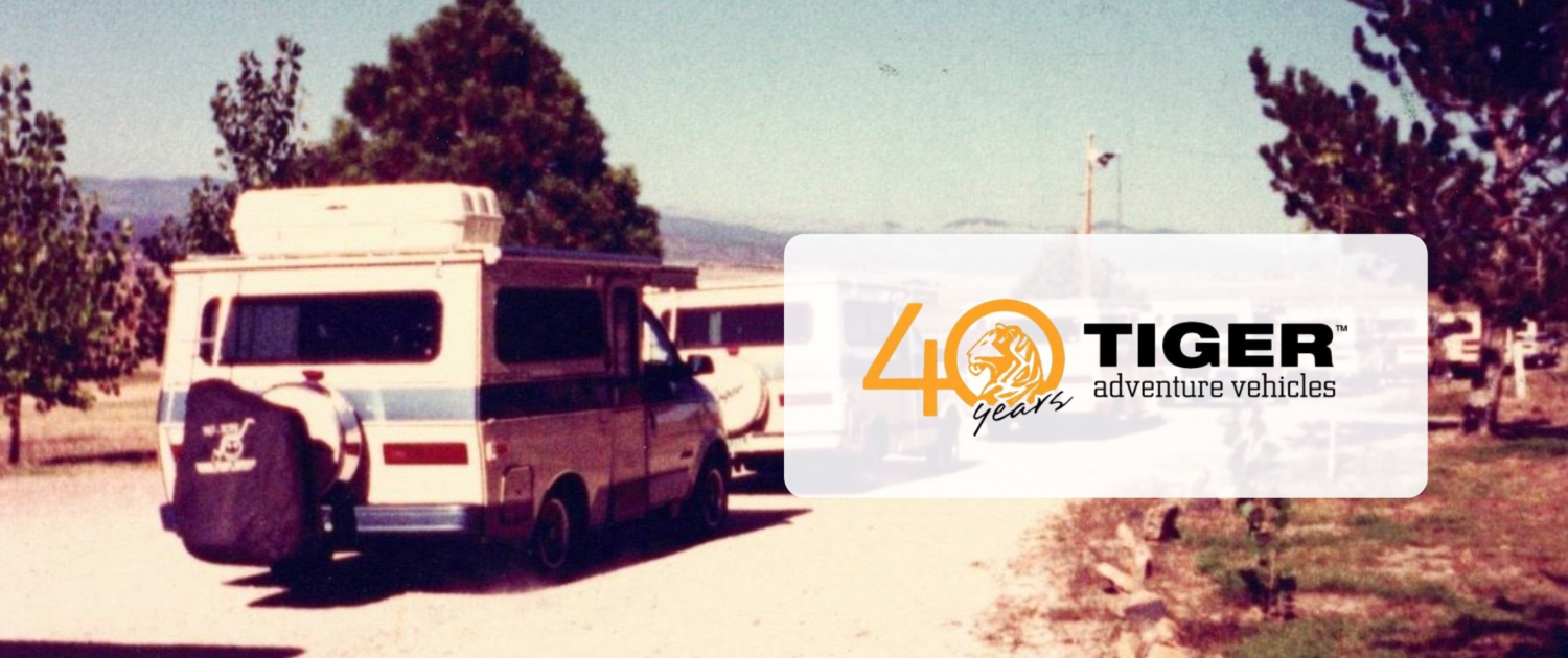 Vintage camper van on a dirt road with trees; translucent overlay reads '40 years' with a tiger logo and 'TIGER adventure vehicles'.