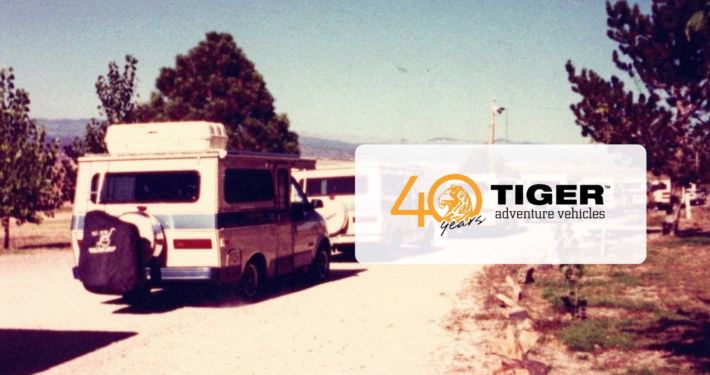 Vintage camper van on a dirt road with trees; translucent overlay reads '40 years' with a tiger logo and 'TIGER adventure vehicles'.