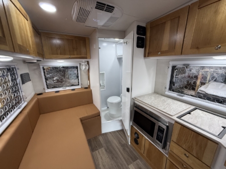 Interior of a compact RV: brown leather seating, wooden cabinets, and a marble-look countertop with a microwave/oven unit.