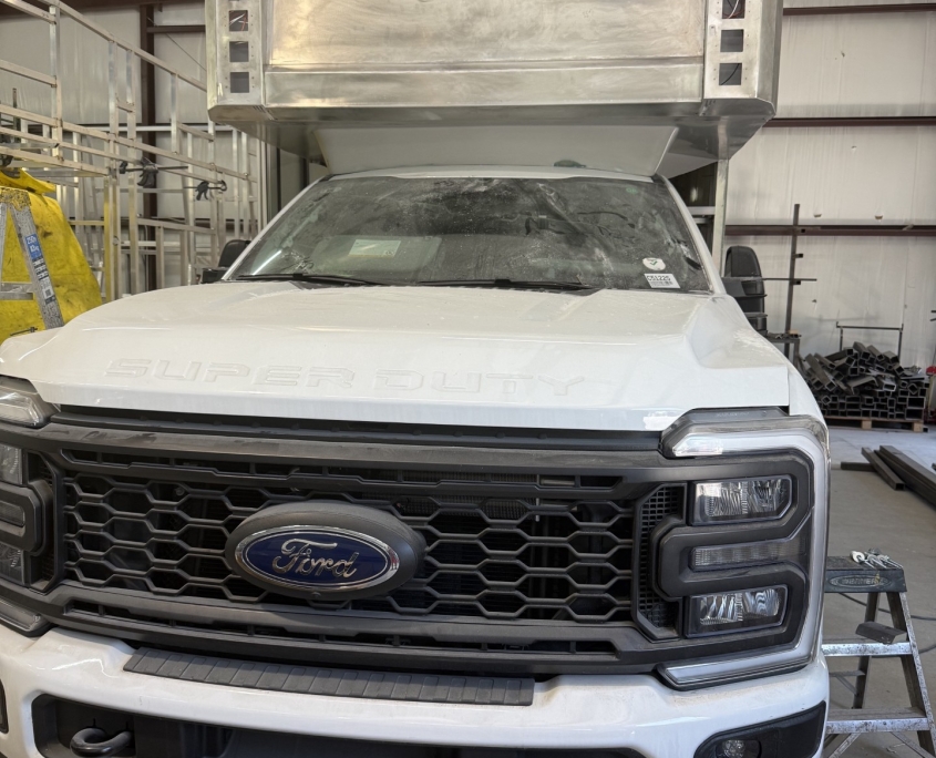 White Ford Super Duty pickup in a shop with a large aluminum utility box mounted on the cab roof for maintenance work
