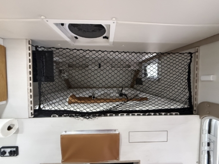 Interior of a small van or camper with a black safety net across a sleeping area, ceiling vent, and storage pockets on the wall.