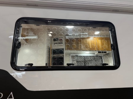 Oven door with glass window and circular dot pattern, showing warm interior with shelves and cabinets beyond the door glass.