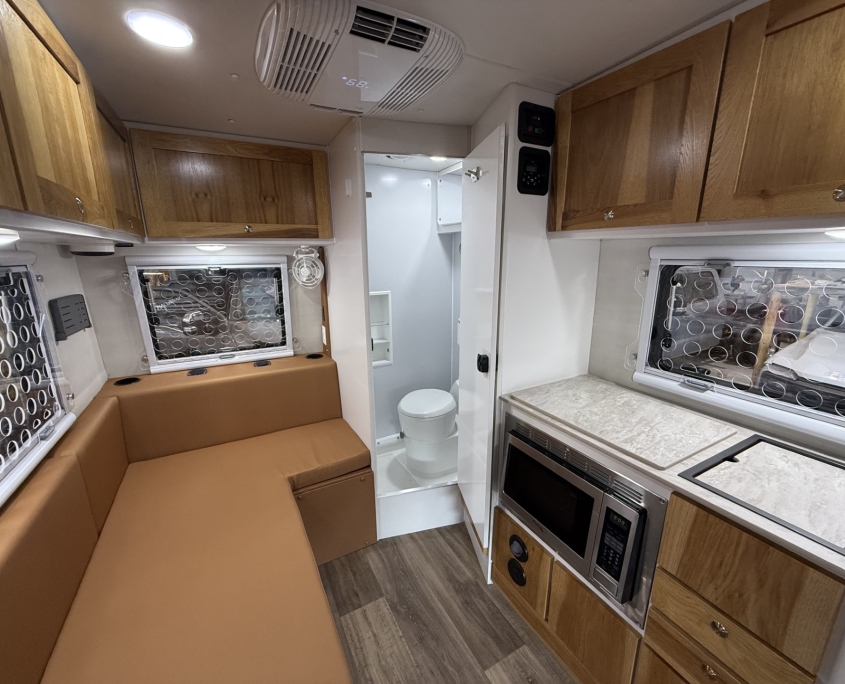 Galley Kitchen with custom windows for pets | Tiger Adventure Vehicles Interior of a compact RV kitchen and living area with brown sofa, wooden cabinets, and a marble countertop kitchenette with a microwave and oven/sink area nearby