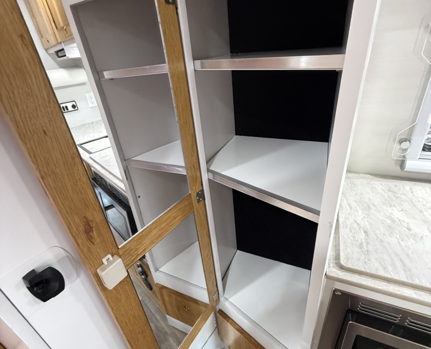 177fe3b8-cd50-4c0f-8c1b-b2aa6194b02c | Tiger Adventure Vehicles Open kitchen cabinet showing white shelves and a black back panel, with a mirrored door reflecting part of the room.