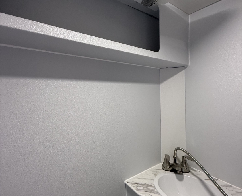 Small bathroom with marble-slab sink and metal faucet, gray walls, and a cabinet above.