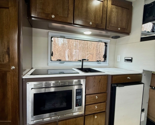 RV kitchen with dark wood cabinets, stainless microwave and oven, and a window above the counter