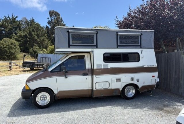White and brown camper van with a raised roof tent parked on a gravel lot.
