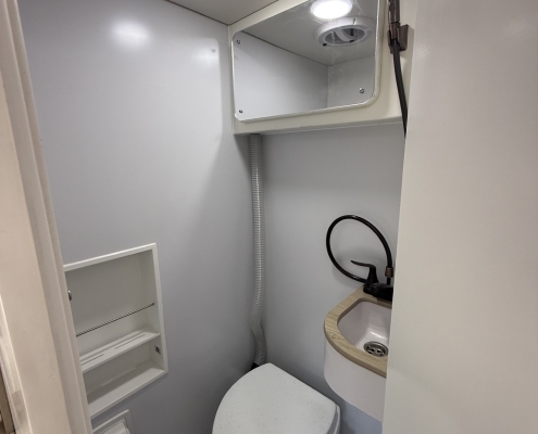 Compact boat head with toilet, small sink and mirror; handheld shower hose mounted on wall.