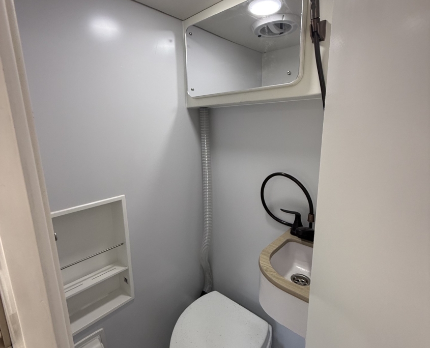 composting toilet | Tiger Adventure Vehicles Compact boat head with toilet, small sink and mirror; handheld shower hose mounted on wall.