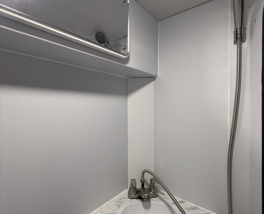 Small bathroom sink with marble countertop, oval white basin, silver faucet, and handheld shower on the right side of the vanity.