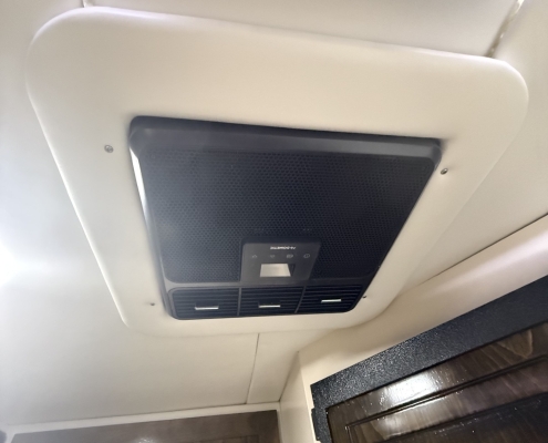 Overhead aircraft cabin ceiling with a dark vent/air grille panel installed in a beige ceiling panel.