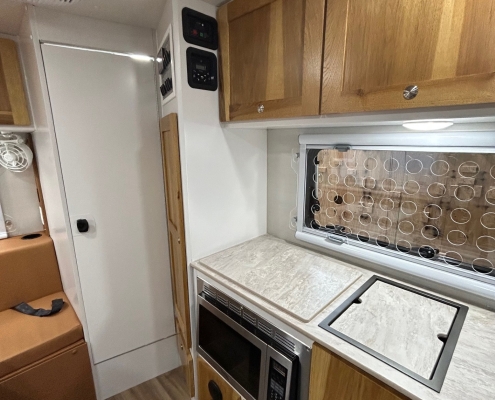Compact RV kitchen with wooden cabinets, stove and microwave built into a marble countertop space