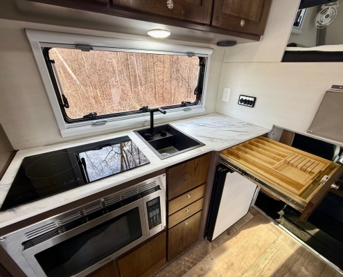 RV kitchen with marble countertop, sink, and stovetop beneath a window showing bare trees outside.
