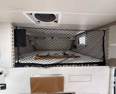 Black mesh safety barrier spanning a doorway in a small vehicle interior, with a round ceiling vent and beige panels above.