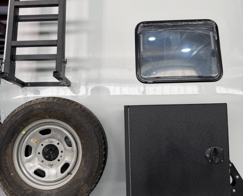 Back of a white trailer with a mounted spare tire, a tall ladder on the left, and a window on the right; Georgia plate GJ1092 visible at the bumper.