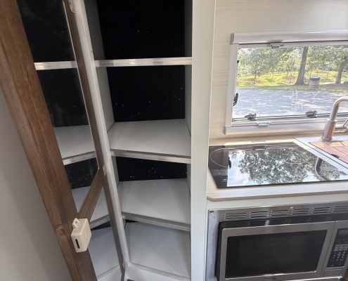 Open kitchen cabinet with empty shelves beside a stainless oven, in a compact RV kitchen.