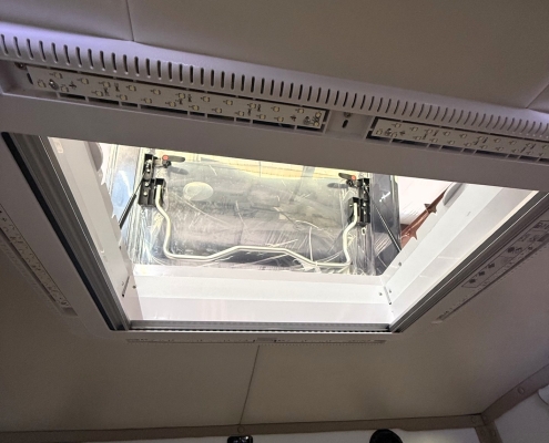 Open ceiling hatch with exposed wiring and panels, viewed from inside a cabin or cockpit area.