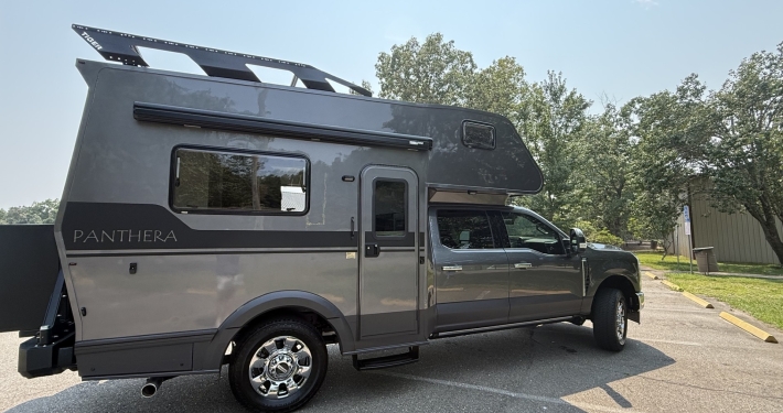 f55cc4b3-b927-4373-9991-0ec3be25b793 | Tiger Adventure Vehicles Grey Panthera motorhome parked in a lot, side view with rooftop luggage rack and large windows
