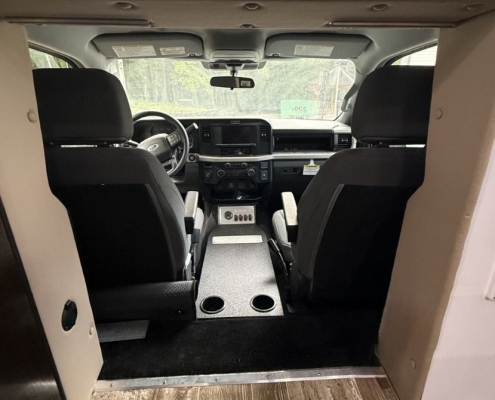 Rear interior view of a vehicle showing two black captain's chairs, a central dash with controls, and two cup holders in the floor between the seats.