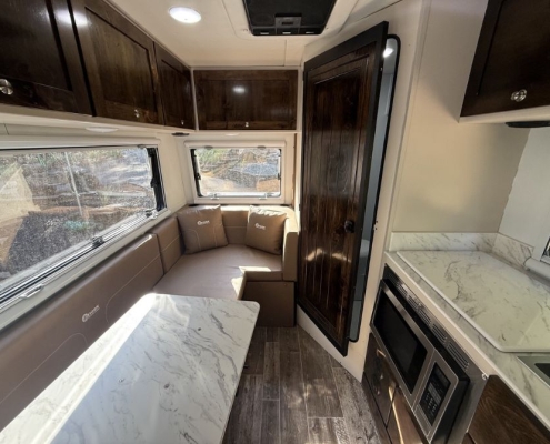 Interior of a compact RV kitchen and lounge with marble-table dinette, beige seating, and dark wood cabinets beneath skylight windows.