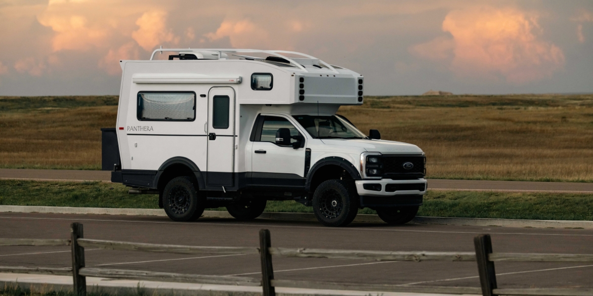 Panthera200-compact-main_img | Tiger Adventure Vehicles White Overland camper truck (Ford) parked on a road with a spacious desert-like plain, tail in the distance, sunset sky in the background.