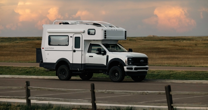 White camper van with a raised roof parked on a rural road against a flat grassland and pastel sunset clouds. (Panthera branding on the side)