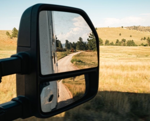 Katie and Joe - New Panthera 200 | Tiger Adventure Vehicles Side-view mirror reflecting a dirt road winding through golden fields and trees in a rural landscape