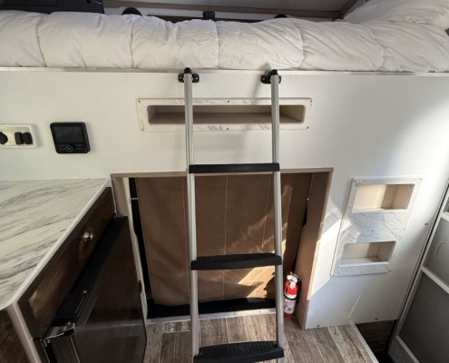 Katie and Joe - New Panthera 200 | Tiger Adventure Vehicles Bunk bed area in a camper with a metal ladder to the top bunk, open storage under the bed, and a fire extinguisher nearby.