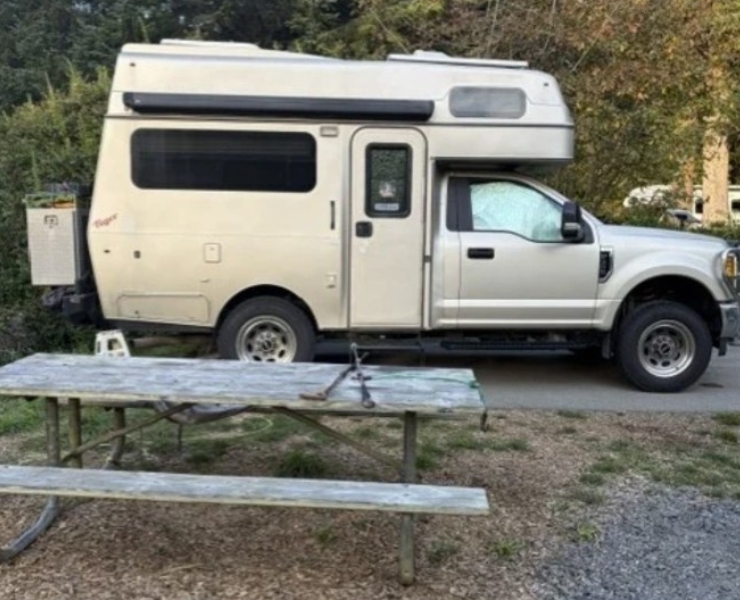 tiger-marketplace-consignment-1 | Tiger Adventure Vehicles White pickup truck with a mounted camper parked beside a wooden picnic table.