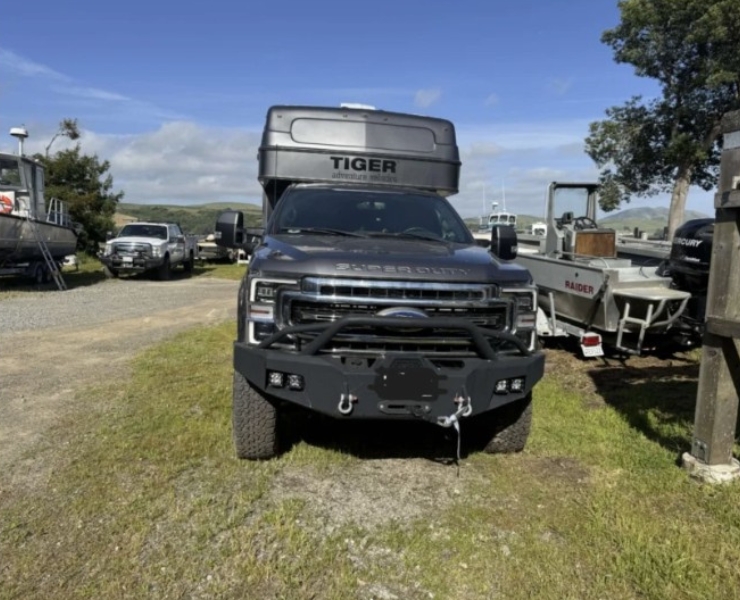tiger-marketplace-consignment-2 | Tiger Adventure Vehicles Ford pickup with heavy-duty front bumper and winches, a TIGER rooftop cargo box mounted on top, parked in a boatyard lot with boats nearby.