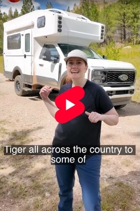 Video thumbnail for 'Introducing the Tiger Pant' with a woman in a cap standing in front of a white camper van in a grassy clearing; a red play button is centered on the image. Overlay text includes 'Introducing the Tiger Pant' and 'Tiger all across the country to some of'.